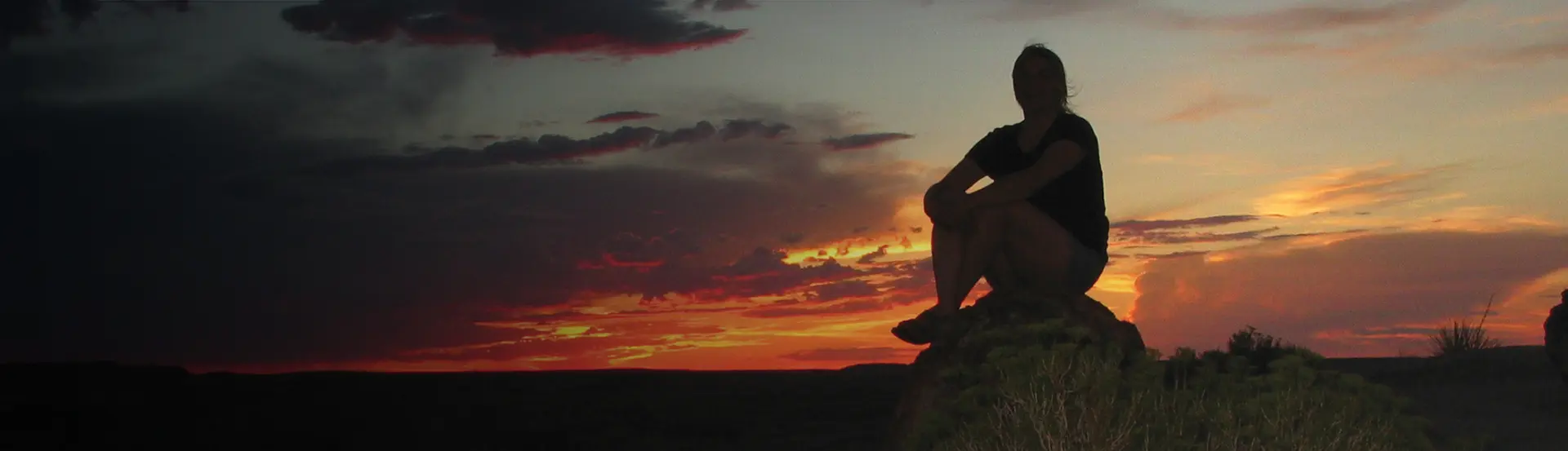A person sitting on top of a hill at sunset.